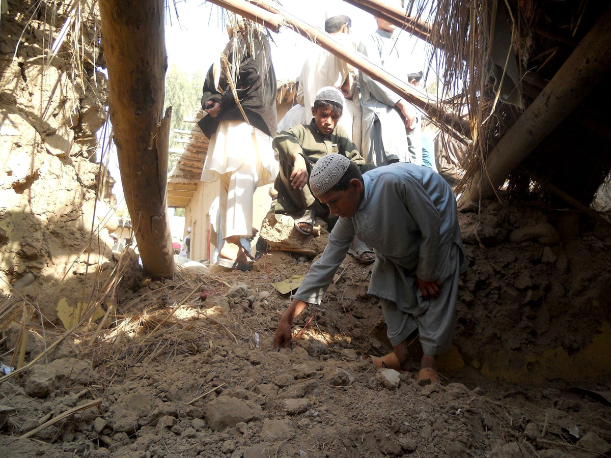 Local residents examine the wreckage of a mud-brick structure in a drone strike's aftermath.
