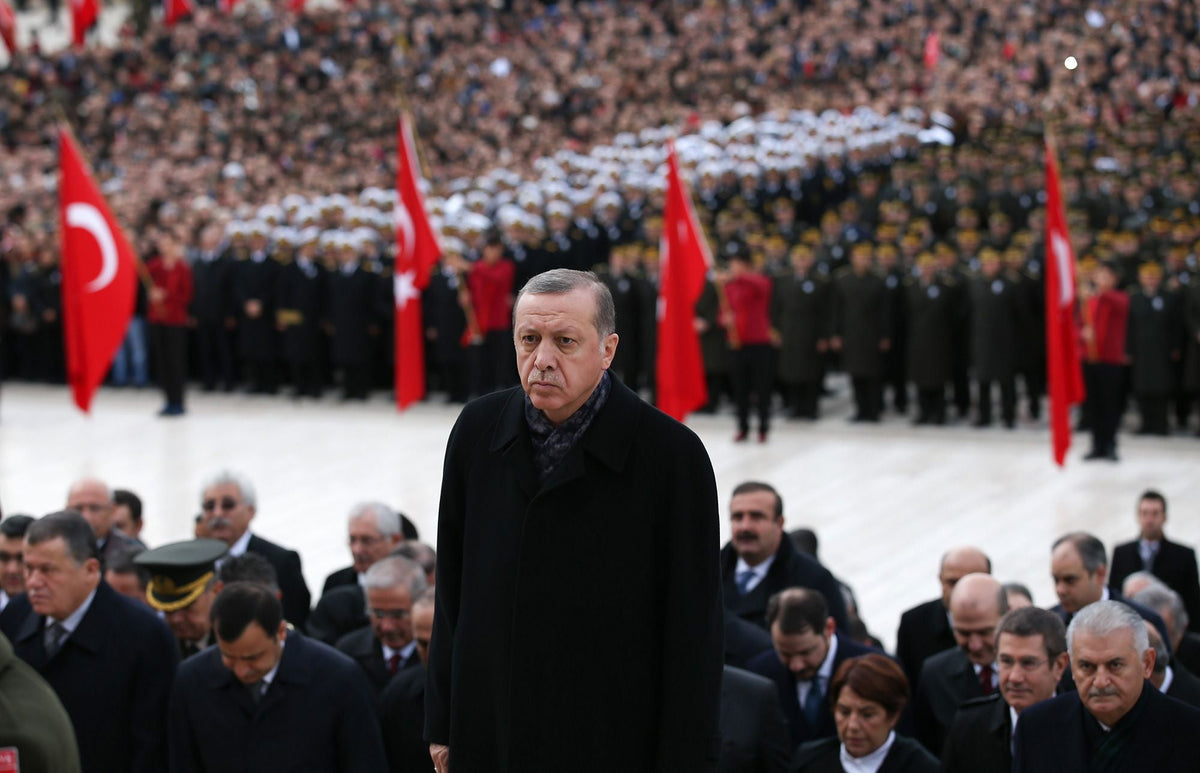 Turkish President Recep Tayyip Erdoğan stands before a crowd with Turkish flags at a state ceremony.