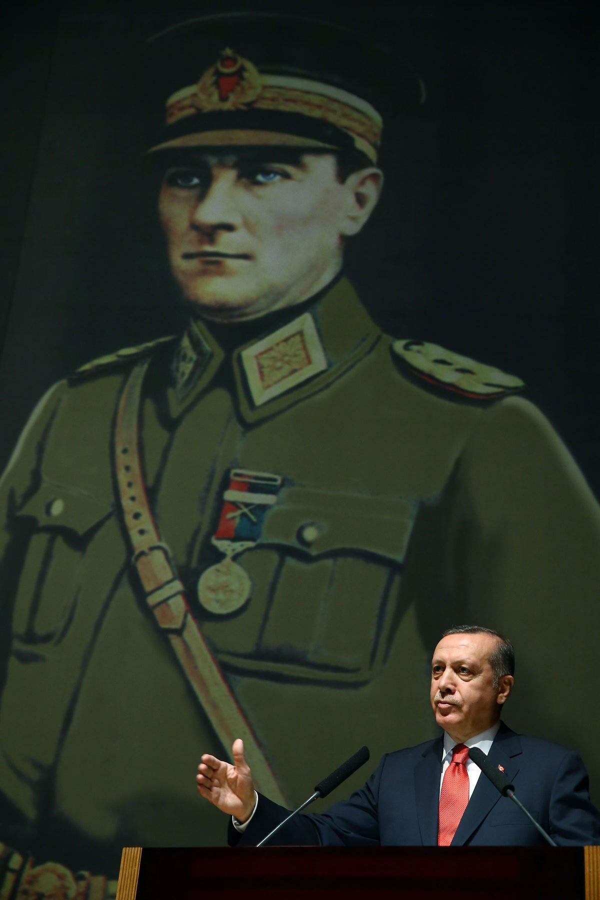 President Erdoğan speaks at a podium beneath a large portrait of Atatürk in military uniform.