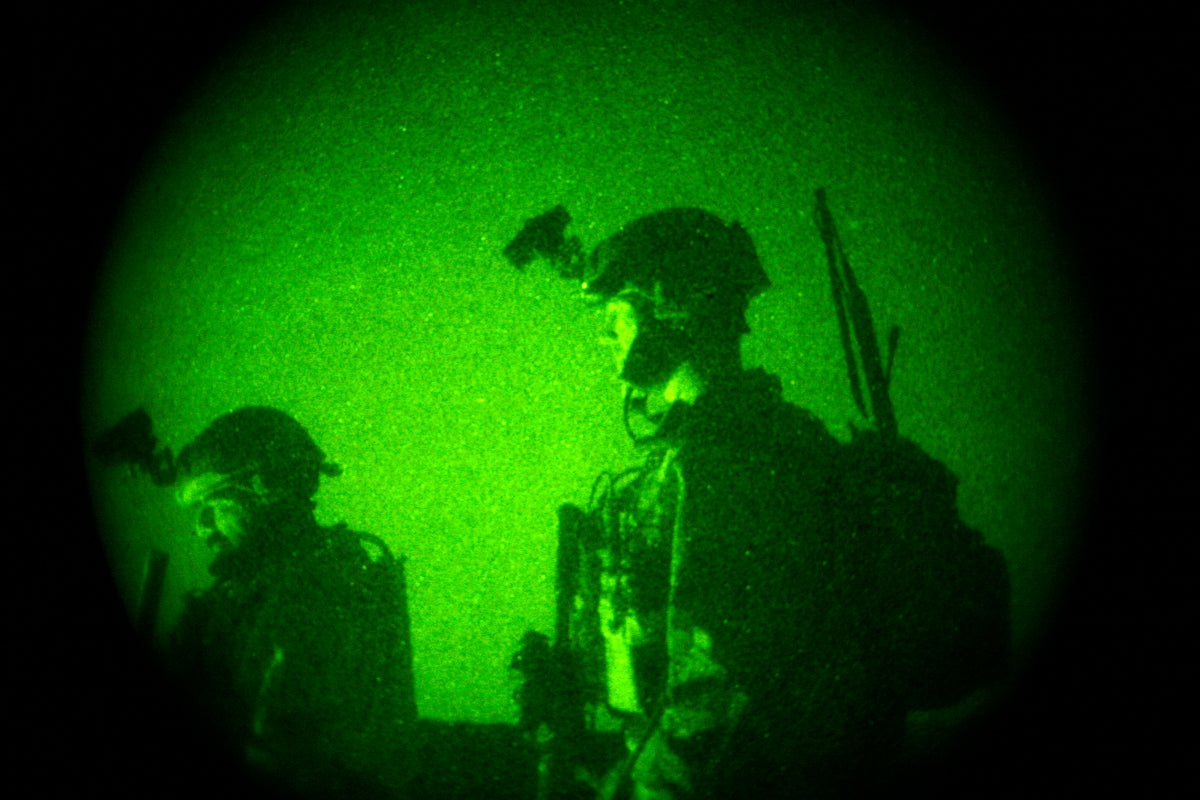 Two special operations soldiers seen through green night-vision optics, wearing helmets and combat gear.
