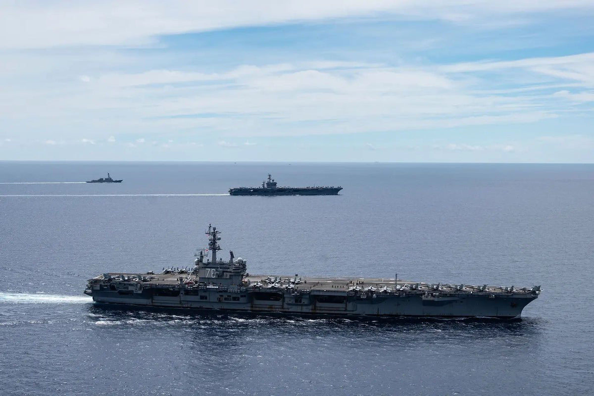 Three U.S. Navy warships, including two aircraft carriers and an escort vessel, sail in formation across the open Pacific Ocean during a naval deployment, illustrating American maritime power and strategic operations in the Indo-Pacific region.