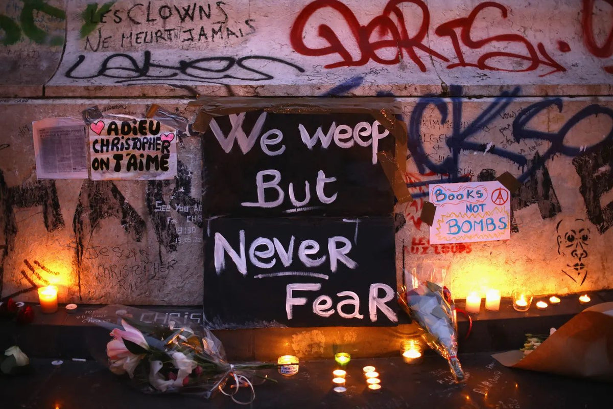 Memorial honoring victims of the November 2015 Paris terrorist attacks, with candles, flowers, handwritten signs, and graffiti-covered walls.