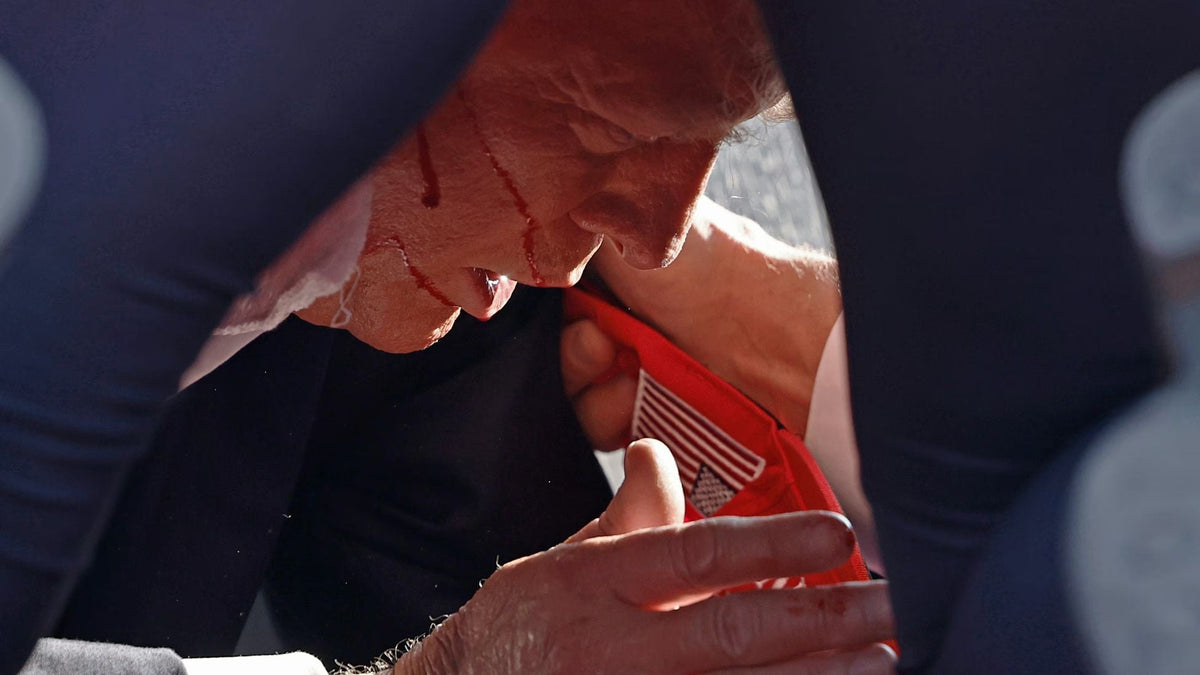 Former President Donald Trump, blood visible on his face after the attempted assassination at a campaign rally in Butler, Pennsylvania, is surrounded by U.S. Secret Service agents as he is escorted from the stage.