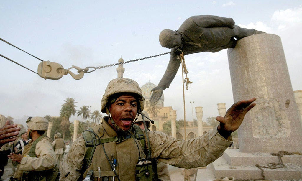 A U.S. Marine gestures as a chain pulls Saddam Hussein’s statue from its pedestal in Baghdad