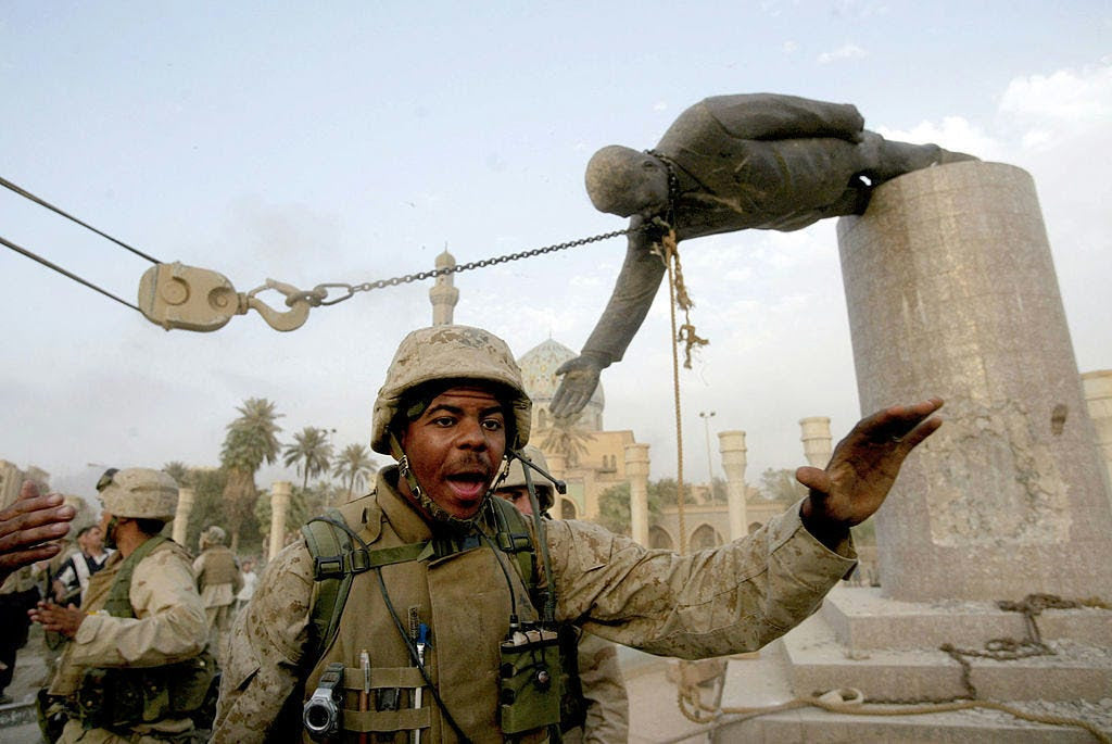 A U.S. Marine gestures as a chain pulls Saddam Hussein’s statue from its pedestal in Baghdad
