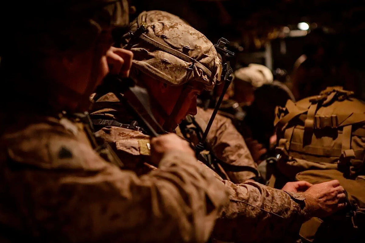 U.S. Marines sit closely together inside a dimly lit military vehicle during a nighttime operation, checking equipment and preparing for deployment.