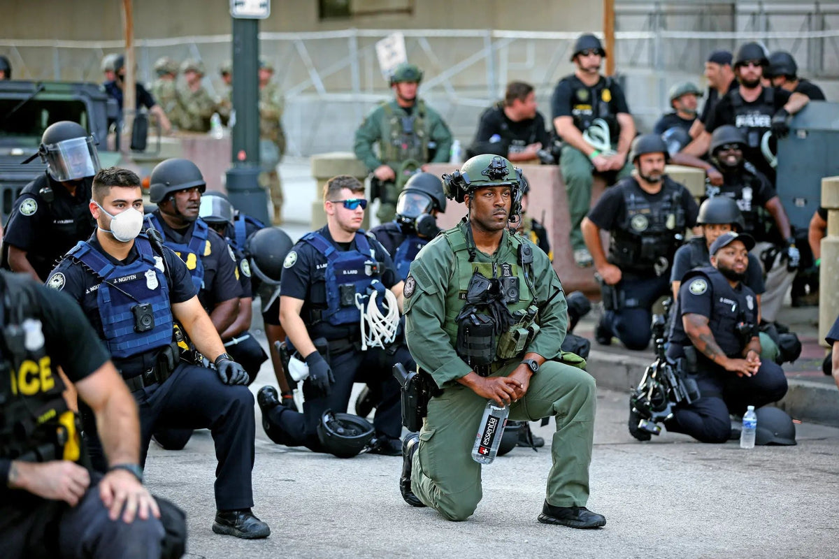 Police officers and tactical law enforcement personnel kneel together during a peaceful demonstration following the killing of George Floyd, symbolizing solidarity with protesters and calls for police reform and community trust.