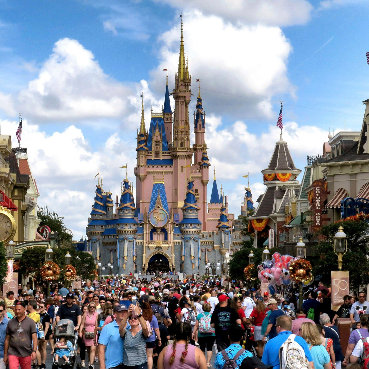 Cinderella Castle at Walt Disney World's Magic Kingdom, seen from a crowded Main Street U.S.A. beneath a partly cloudy sky.